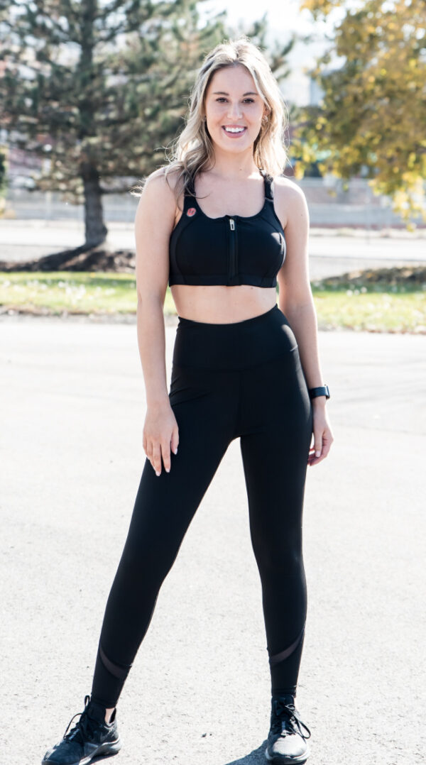 A woman walking wearing a sports bra and black high rise leggings